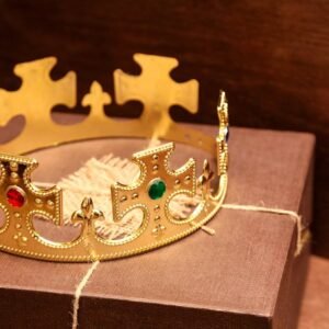A luxurious gold crown with gems sits atop a brown gift box in a rustic setting.